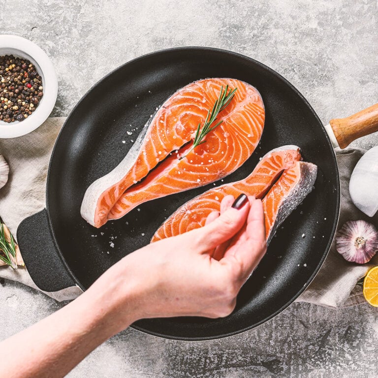 Chef salts raw salmon steak in a frying pan. Healthy seafood. Gr