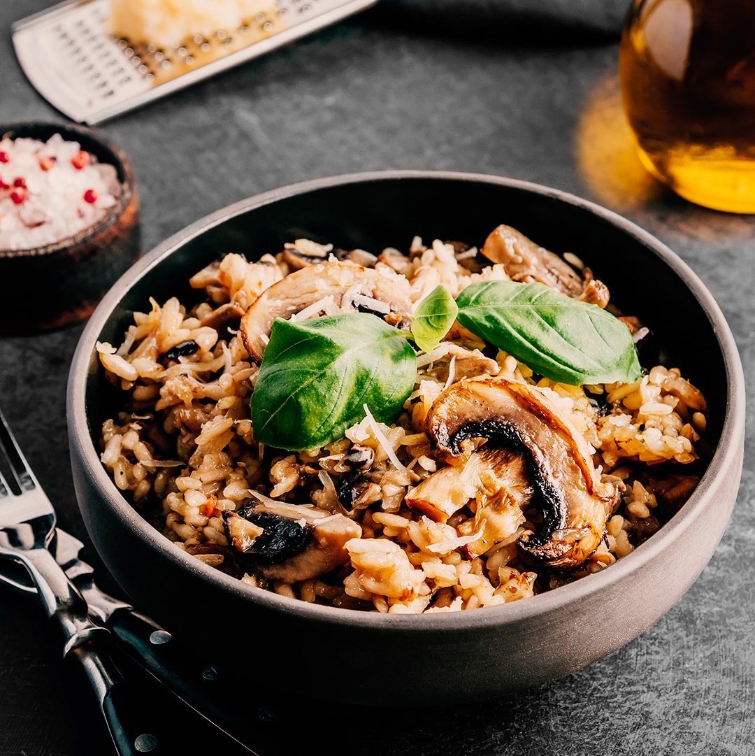 Traditional italian risotto with mushrooms and parmesan cheese on a dark bowl on a black table.